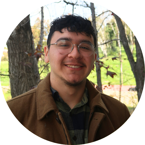 Man smiling with glasses. Trees in the background.