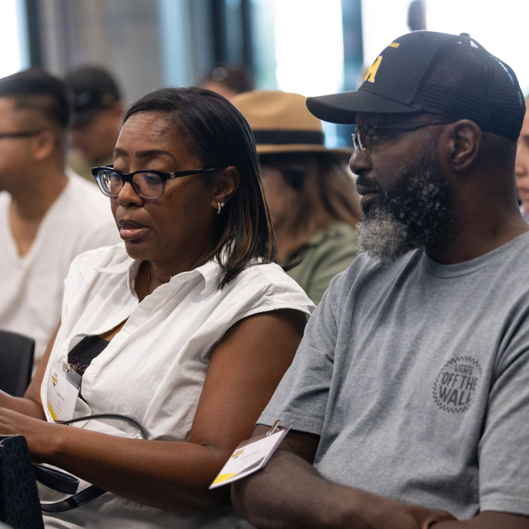 Two adults sit side by side in what appears to be a group setting or workshop. 