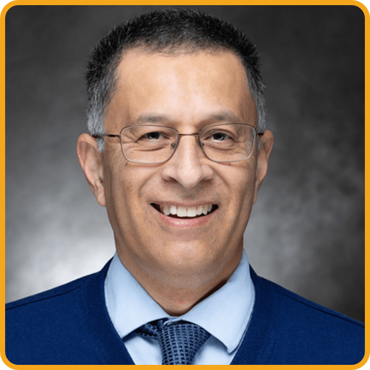 Headshot of Paul Gomez with a golden border. He is smiling and wearing a blue sweater with a blue tie.