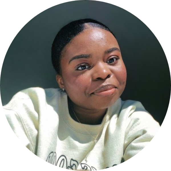 Woman smiling with a cream colored sweatshirt and a shaded background.