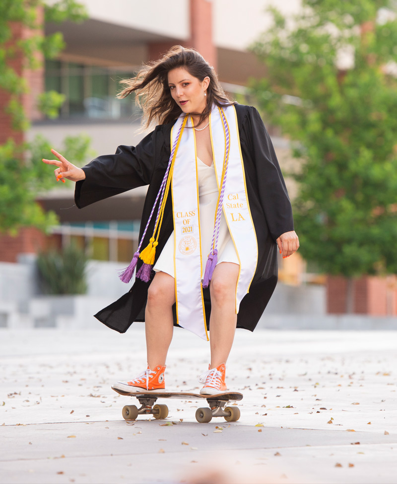 A graduate posing for a photo on a skateboard.