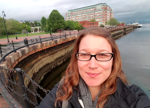 Young woman taking a selfie with the Boston harbor behind her.