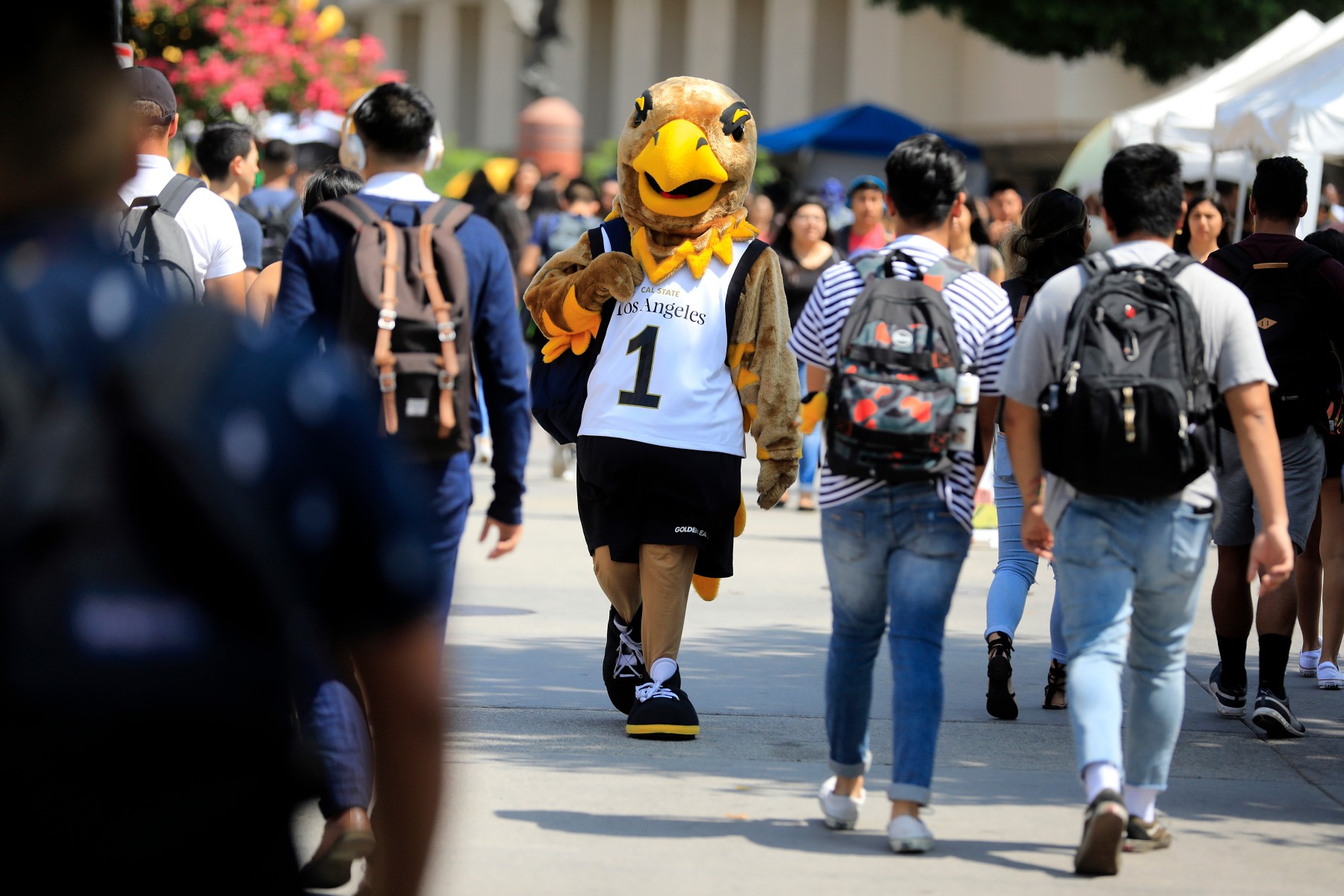 Eddie the Eagle walking with backpack in crowd outdoors