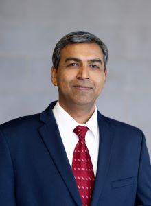 Photograph of Andre Ellis wearing a navy blue coat, white shirt and red tie