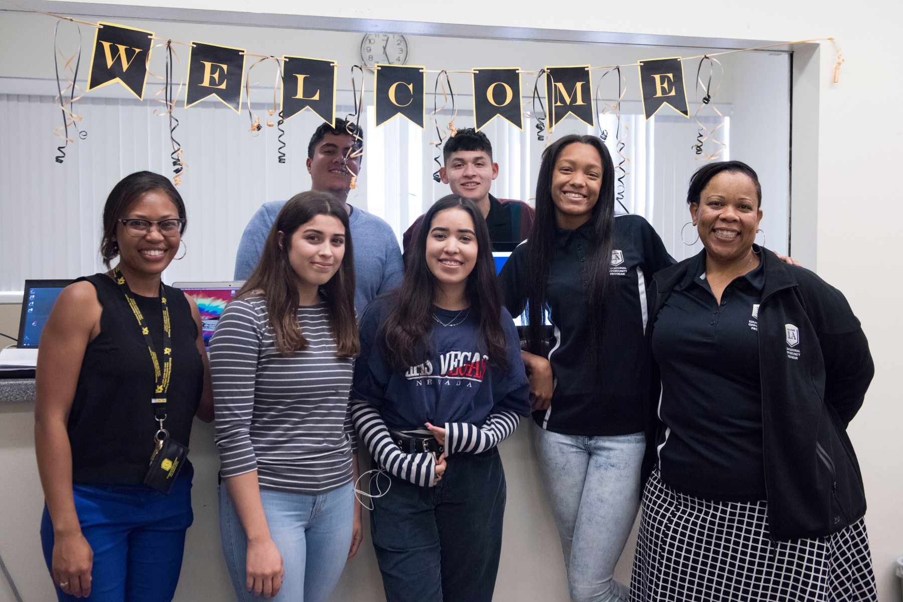 Two staff members stand with a group of five students under a welcome banner