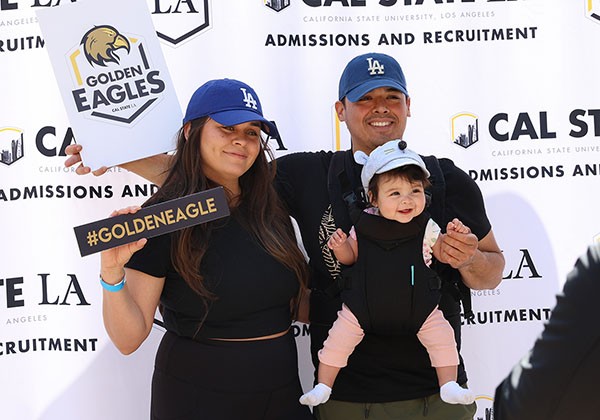 Two adults with a baby posing in front a step and repeat for Admissions and Recruitment.