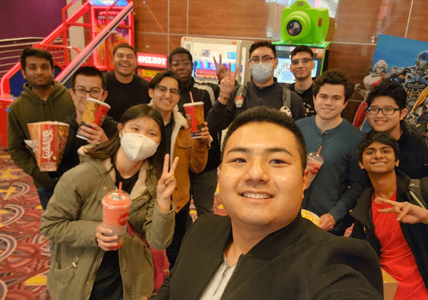 A group of men and women smiling in front of bright video games in a theater.