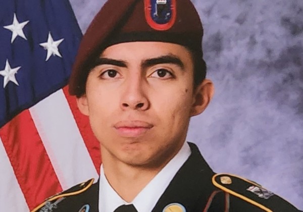 A person in a military uniform in front of an American flag.