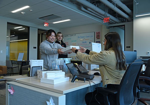 Student picking up a laptop from the front desk of a lobby.