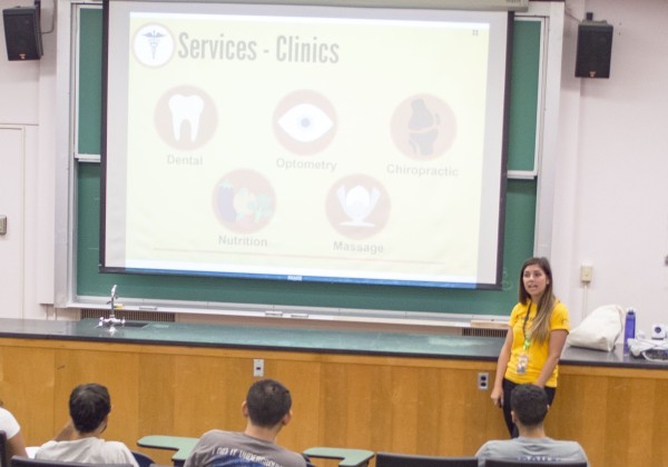 A student in a yellow polo standing in front of a screen with a health services presentation.