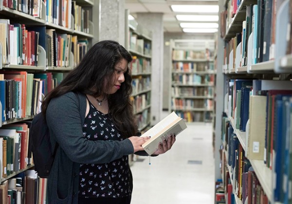 Woman standing in between bookstacks looking at an open book