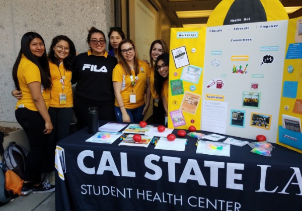 Six student interns in yellow shirts behind outreach table.