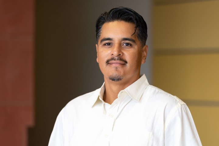 Gregorio Pacheco wearing a white cream colored dress shirt in front of a yellow wall