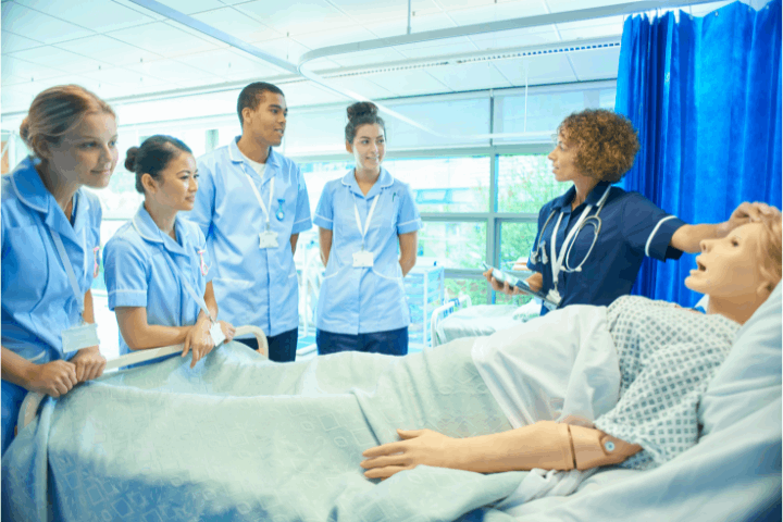 Instructor with nursing students at bedside in hospital.