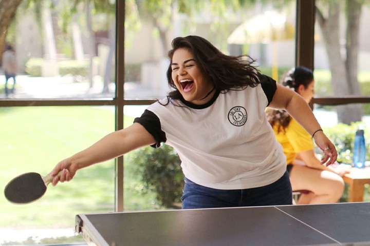 Cal State LA student smiling while playing ping pong indoors during a campus activity.