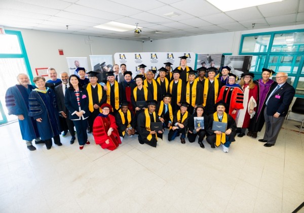 Graduates and faculty members pose together in academic regalia during a Prison Graduation Initiative ceremony at Cal State LA. 