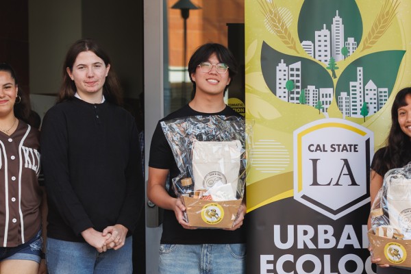 A group of students stands beside a Cal State LA Urban Ecology banner, holding gift bags and smiling at the camera.