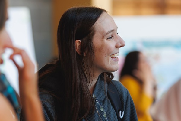 A young woman smiles while engaging in a conversation at the event, with people in the background.