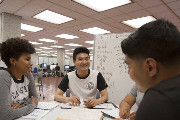 Group of students gathered in the library around a dry-erase board, studying. 