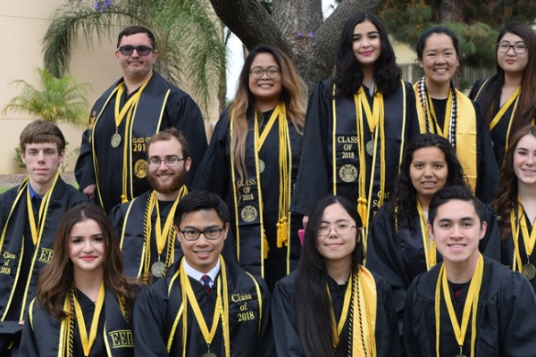 Group of Honors College graduating students in Commencement regalia, gathered in front of the jacaranda tree on campus. 