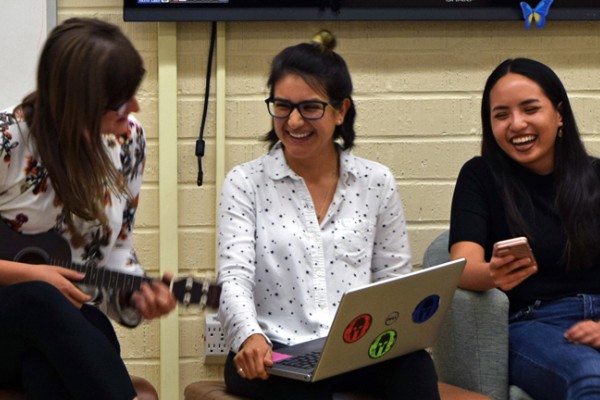 Three female students smiling, one playing a ukalele. 