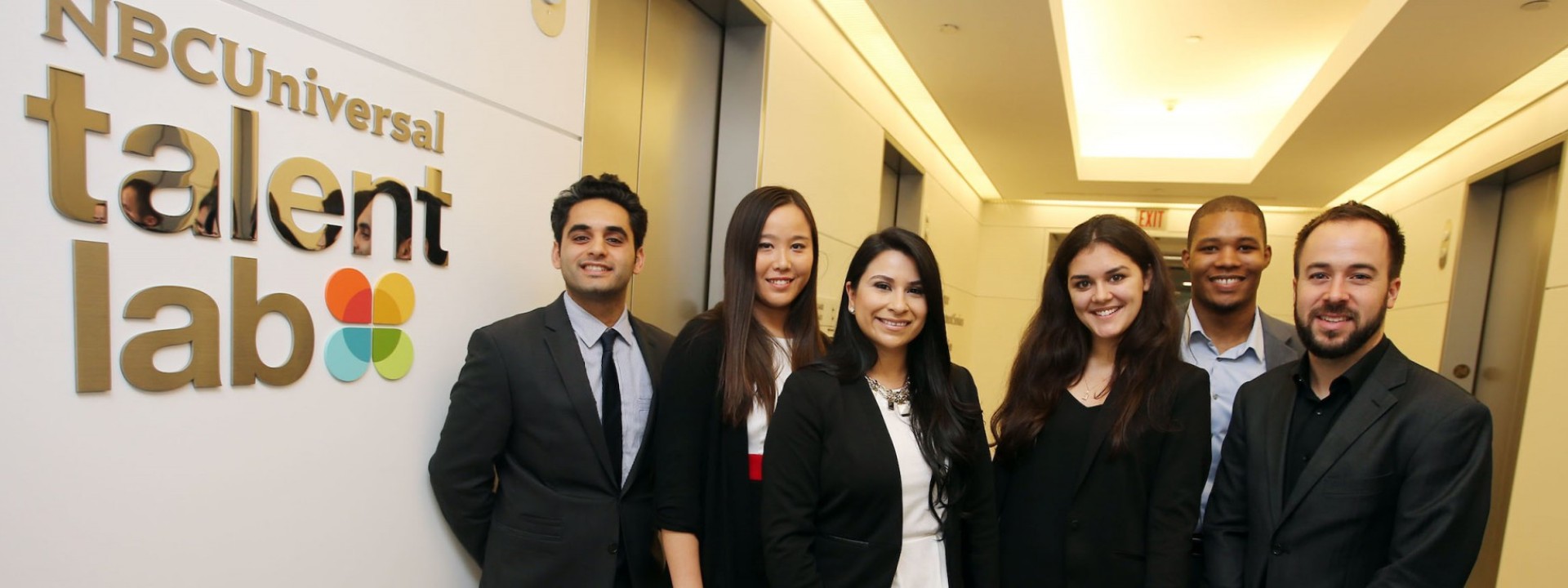 Group of Cal State LA students in business attire standing grouped in front of the NBC Universal Talent Lab sign. 